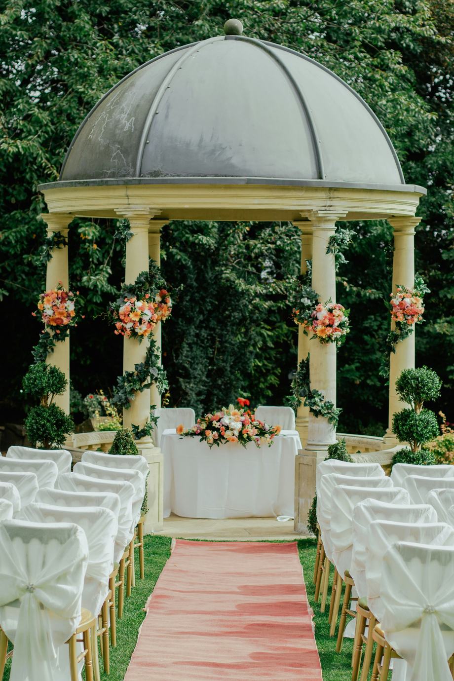 An outdoor ceremony pavilion with flowers and white chairs